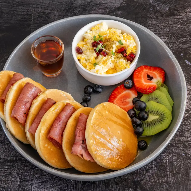 American pancakes with turkey rashers, scrambled egg, fresh berries and a jug of maple syrup.
