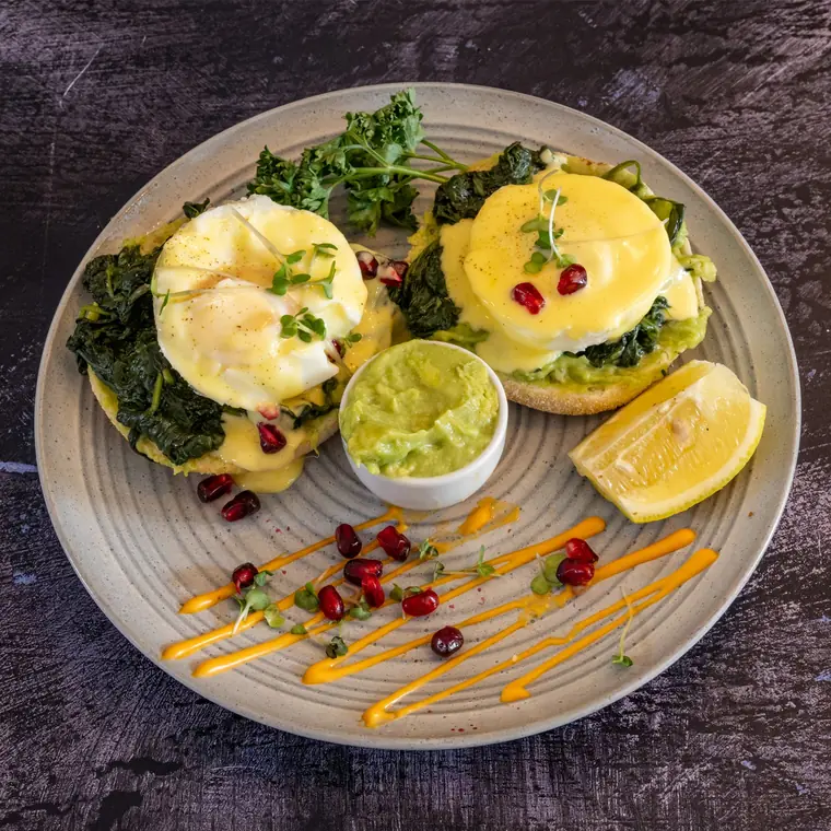 Two poached eggs on muffins with spinach, hollandaise and pomegranate seeds.
