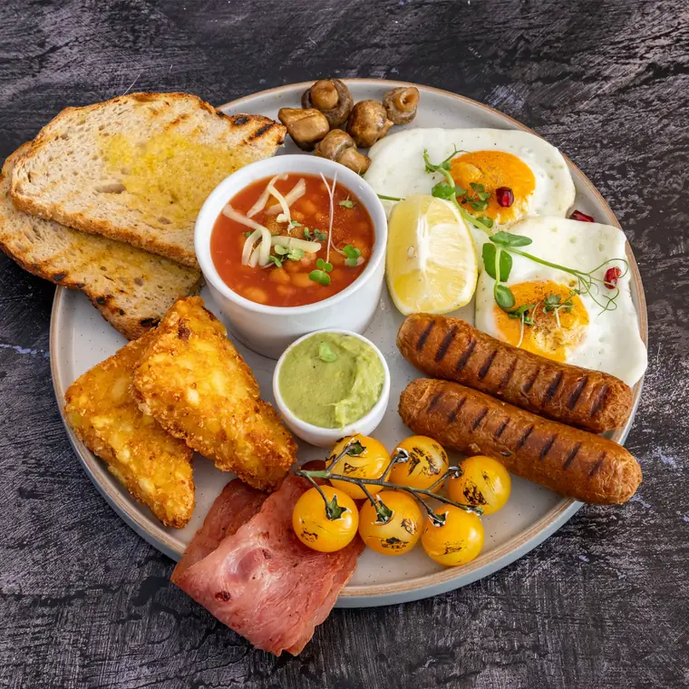 The full English at TenTen — chicken sausages, turkey rashers, halloumi, beans, grilled tomatoes and toast on a wide grey plate.