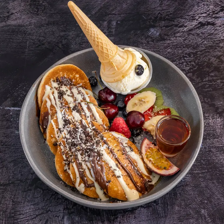 Stack of fluffy pancakes with fresh fruit, a scoop of vanilla ice cream and maple syrup.