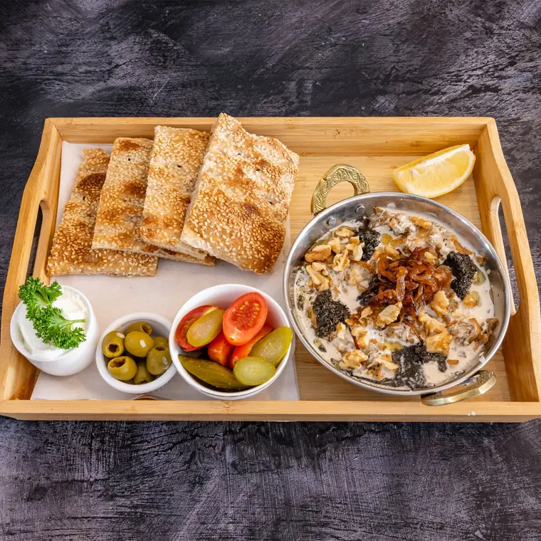 Persian aubergine and walnut dip with flatbread, olives and pickles on a wooden tray.